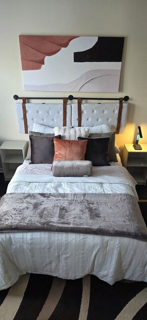 Un lit avec une tête de lit capitonnée, plusieurs oreillers et un tapis  à motifs rayés.