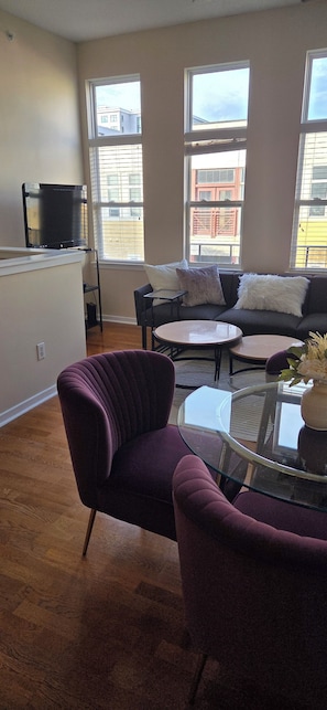 A living room with a purple armchair, a glass coffee table, and a sofa with cushions. - Fantastic 1-Bedroom Condo in Southend! (CHARLOTTE)