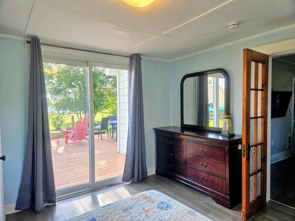 A room with a sliding glass door leading to an outdoor deck, a dark wooden dresser with drawers, and a large mirror.