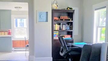 Una habitación con una silla de oficina negra, una estantería con juguetes y una ventana.
