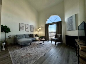 A living room with a sofa, armchair, coffee table, and a large window with curtains. - Stylish 2 bedroom + loft with rooftop patio and views near Beverly Hills (Beverly Hills)