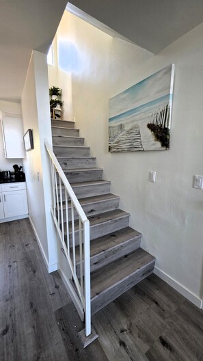 A staircase with a white railing leading to a landing, a painting of a pier on the wall, and a kitchen area with cabinets and a countertop. - Stylish 2 bedroom + loft with rooftop patio and views near Beverly Hills (Beverly Hills)