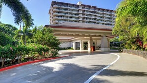 Ein Hotel mit Eingangsbereich, einer überdachten Laue, Palmen und einem mehrstöckigen Gebäude im Hintergrund.