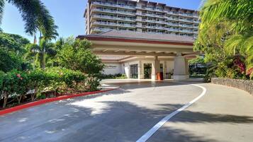 Ingresso di un hotel con una tettoia, palme e un edificio a più piani sullo sfondo.