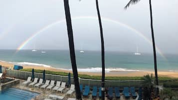 Une vue sur la plage avec une piscine, des chaises longues et un arc-en-ciel bien visible.