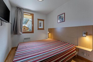 Ein Schlafzimmer mit einem Bett, einem Fenster, einem Wandbild und einem Nachttisch mit einer Lampe.