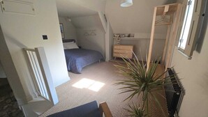 Une chambre à coucher avec un lit, une commode, un miroir, une plante en pot et un luminaire suspendu.