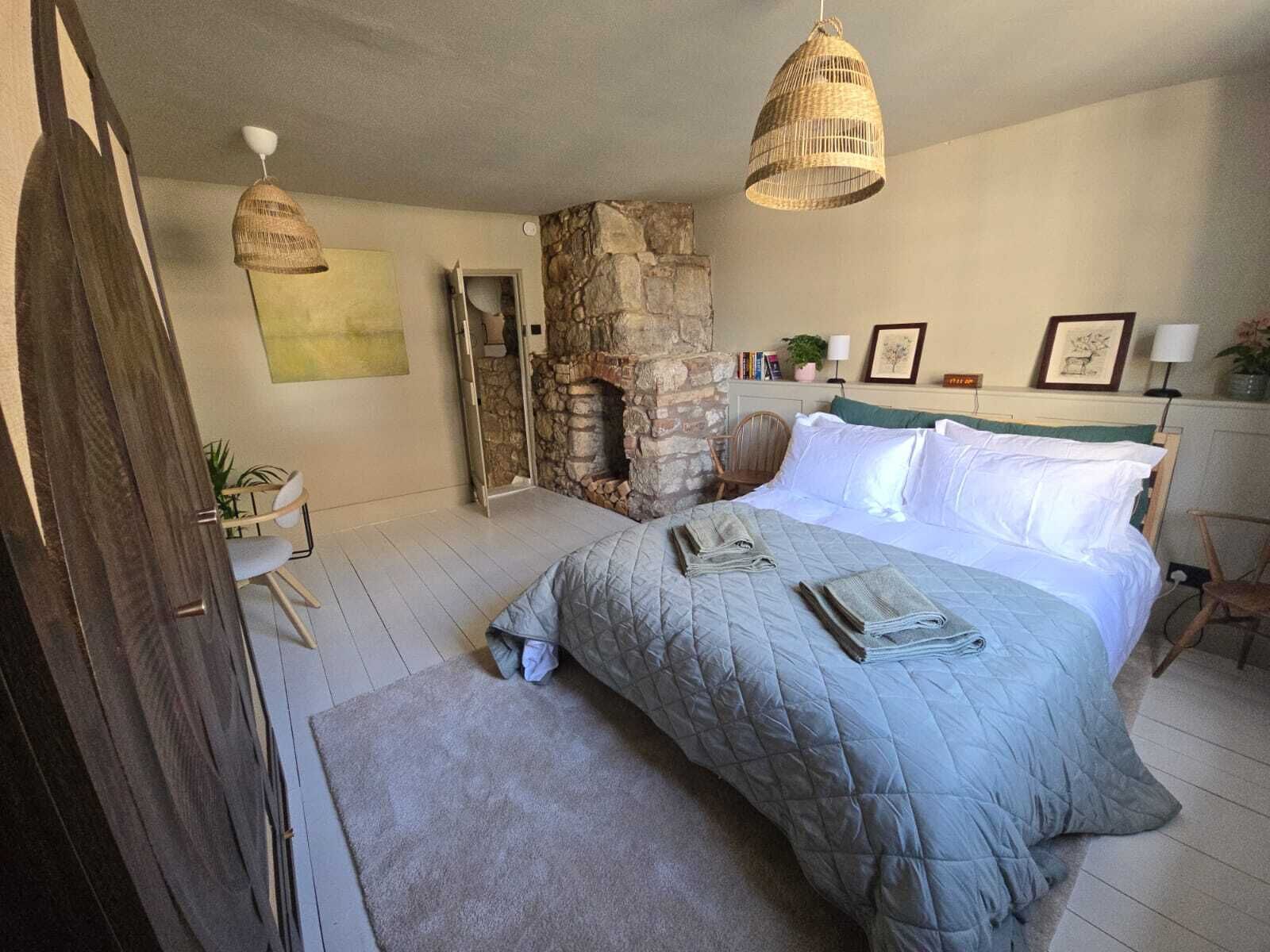 A bedroom with a stone fireplace, a bed with a quilted duvet, and two hanging wicker lamps.