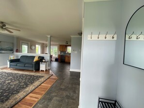 A spacious living area with a dark-colored sofa, a patterned rug, and a kitchen in the background. - PEI Cozy Clean Cottage with Hotub (Summerside)