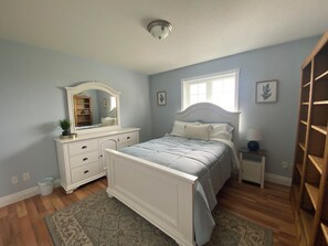 A bedroom with a bed, dresser, mirror, bedside table, and a window. - PEI Cozy Clean Cottage with Hotub (Summerside)