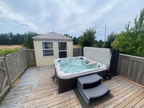Een hottub op een houten terras, met een kleine schuur op de achtergrond.
