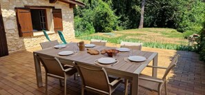 Ein Essbereich im Freien mit einem Steinhaus, einem Tisch für vier Personen und Stühlen.