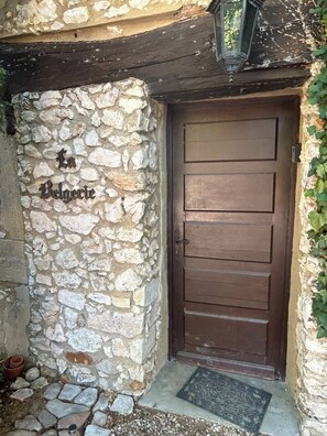 A stone wall with a wooden door and a metal doormat. - Belgerie in the Gard Department (Saint-André-de-Roquepertuis)