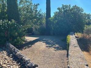 Uma trilha de cascalho serpenteia por um jardim com muros de pedra e diversas plantas.
