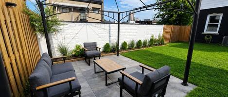 Une terrasse extérieure dotée d’une pergola, d’un espace salon et offrant une vue sur un immeuble d’habitation.