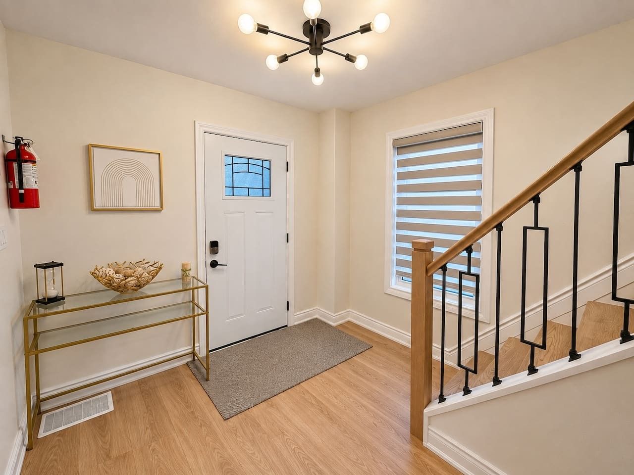 A hallway with a white door, a glass console table, a fire extinguisher, and a staircase with a wooden handrail.