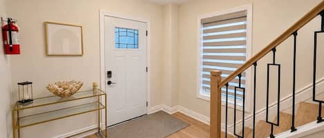 A hallway with a white door, a glass console table, a fire extinguisher, and a staircase with a wooden handrail.