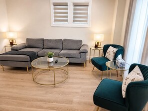 Un salon moderne avec un canapé gris, deux fauteuils, une table basse en verre et deux petites tables d’appoint avec des lampes.
