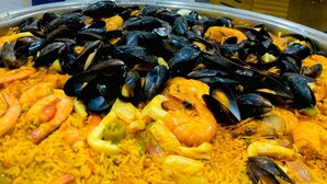 Paella de mariscos con mejillones y camarones, zona de bufé con mesas y sillas, y una pared decorada con globos.