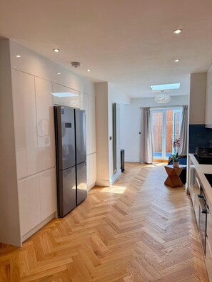 Eine moderne Küche mit integriertem Kühlschrank, Holzdielenboden und Blick ins Freie.
