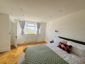 Een slaapkamer met een bed, een raam met gordijnen, een radiator en een nachtkastje.