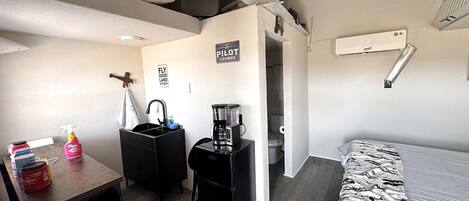 Une chambre compacte comprenant un lit, une petite table avec une machine à café, un lavabo et un espace douche.
