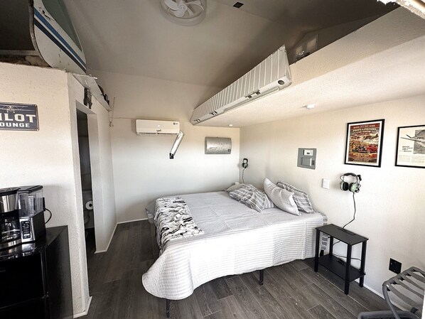 A compact hotel room with a bed, a small desk, a chair, and a coffee machine.