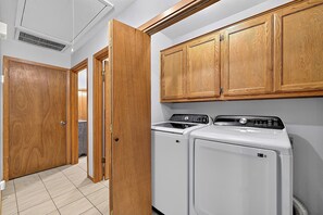 A laundry area with two white front-loading washers and dryers, wooden cabinets above, and a tiled floor.