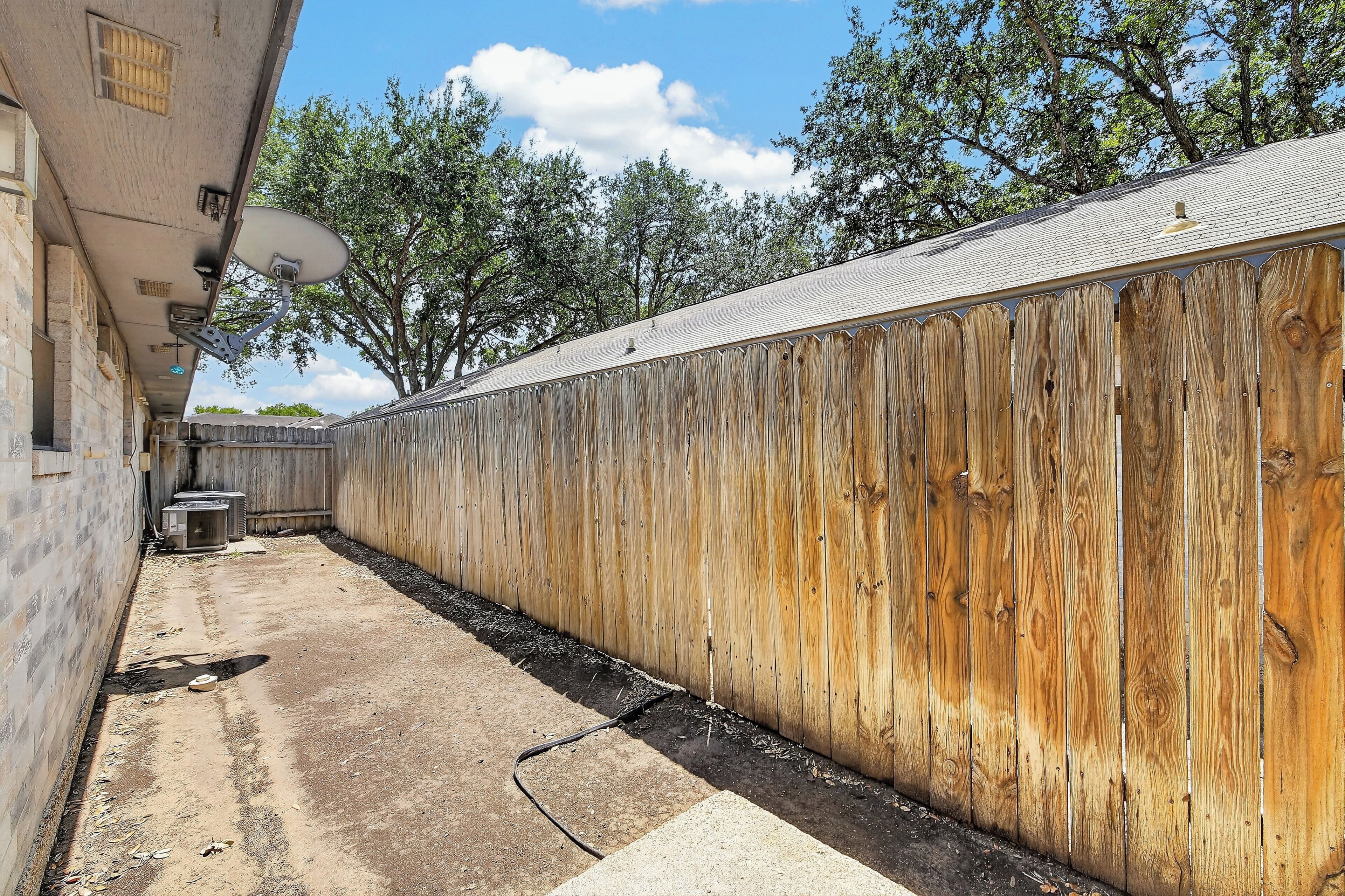 A fenced outdoor area with a concrete path, a satellite dish, and a trash bin.
