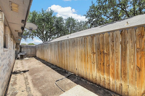 A fenced outdoor area with a concrete path, a satellite dish, and a trash bin.