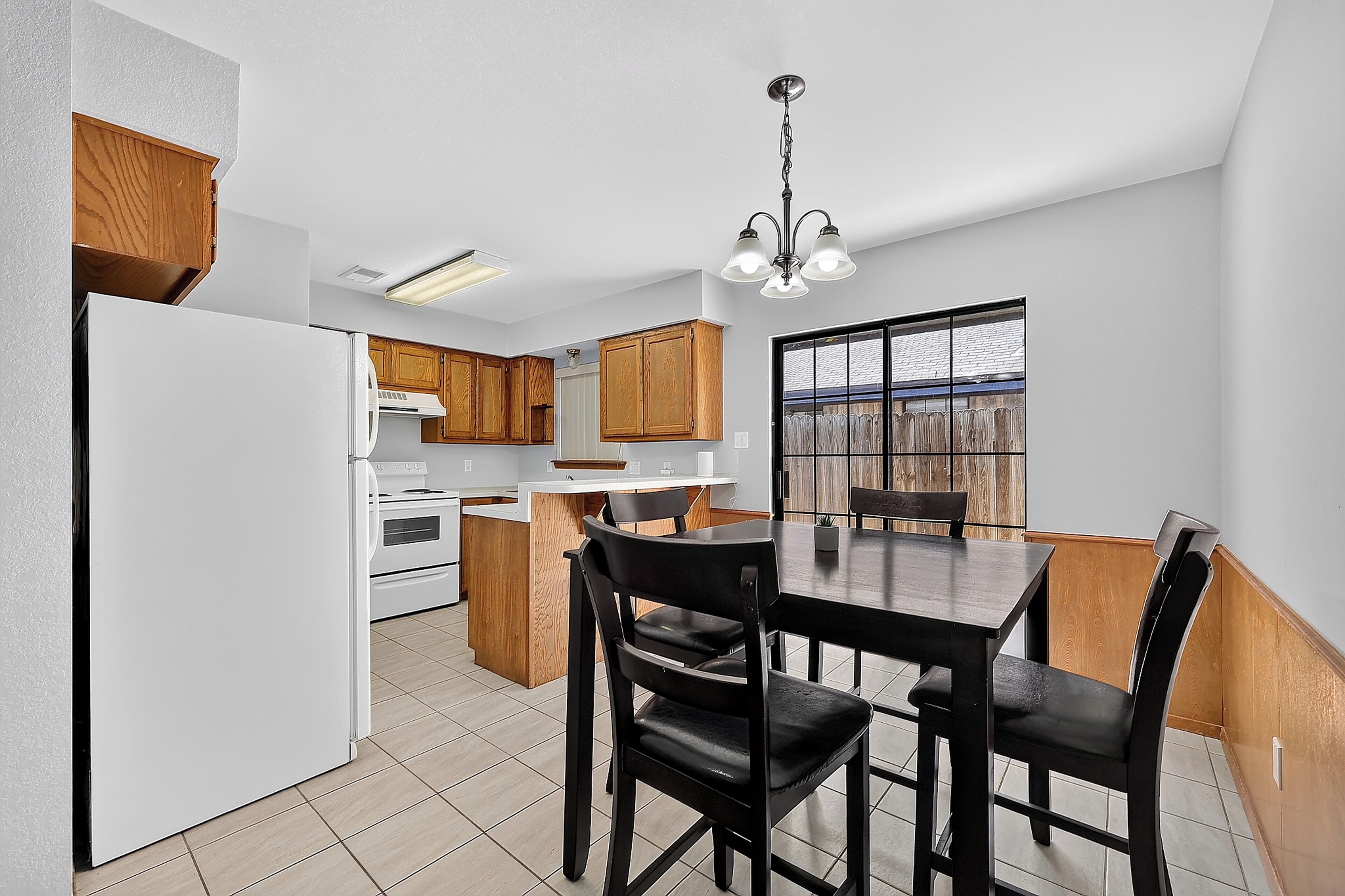A compact kitchen with white appliances, wooden cabinets, and a dining area with a table and chairs.