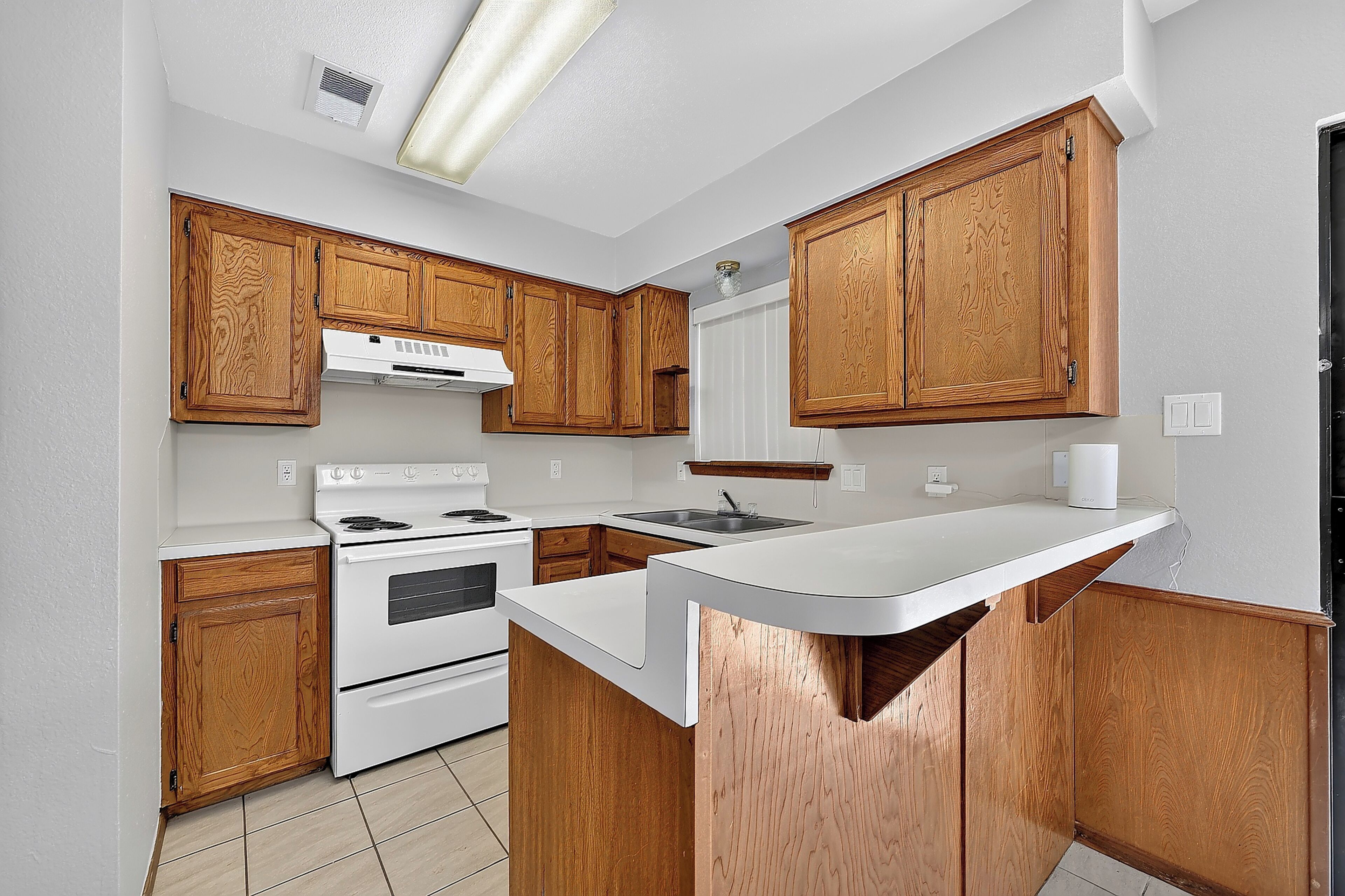 A kitchen with wooden cabinets, a white countertop, a stove, and a sink.