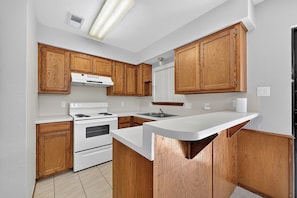 A kitchen with wooden cabinets, a white countertop, a stove, and a sink.