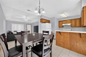 A modern kitchen with wooden cabinets, a dining table with chairs, a ceiling fan, and a built-in oven.