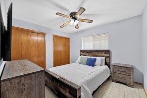 A bedroom with a bed, wooden wardrobe, a television, a ceiling fan, and a window with blinds. - Cozy North McAllen Condo - Walk to Bill Schupp Park - 103" Theater (McAllen)