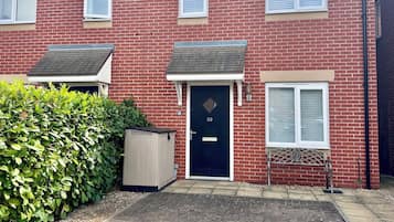 Una casa de ladrillo de dos pisos con puerta principal, dos ventanas, una chimenea y un pequeño jardín delantero.