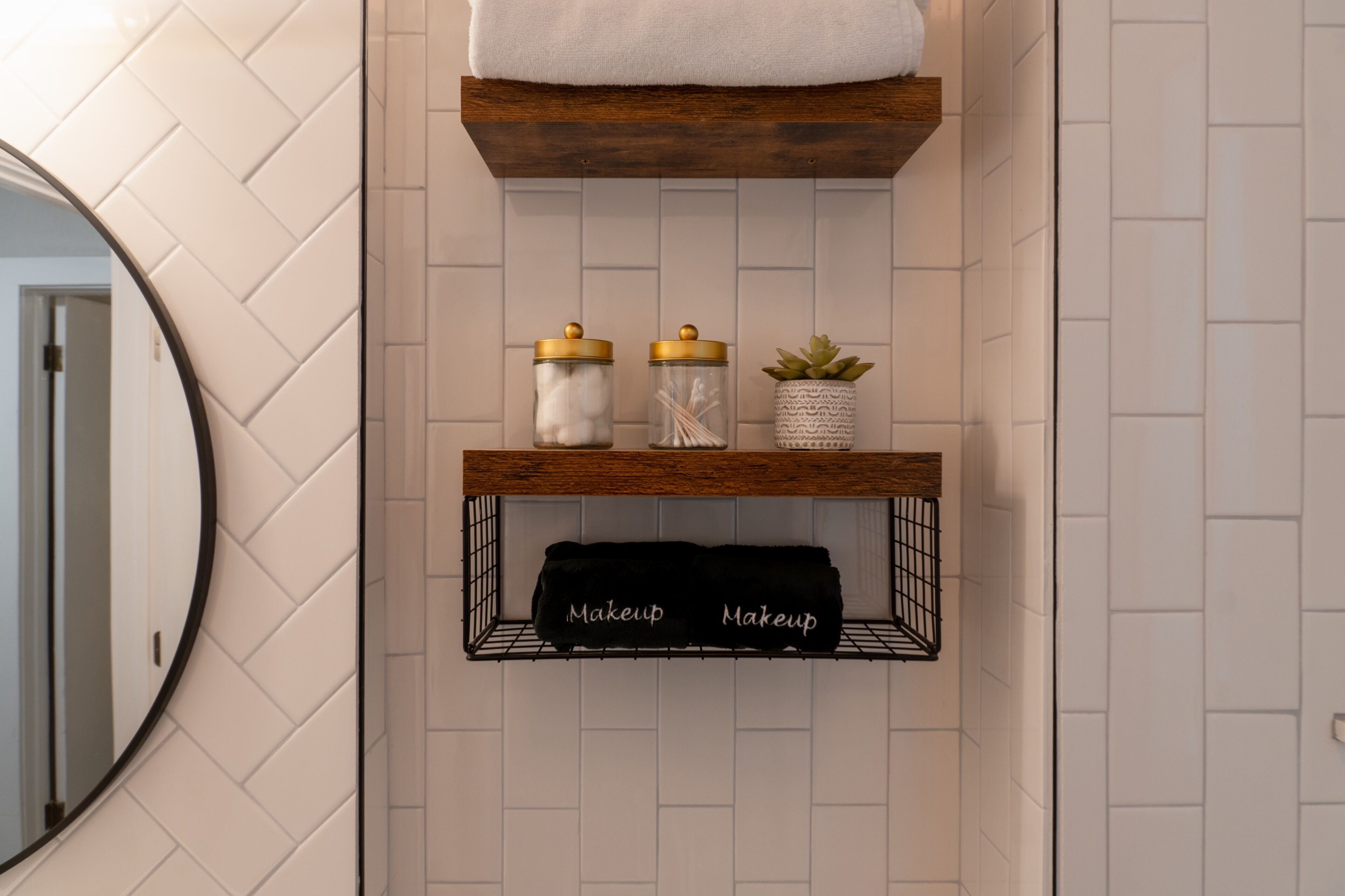 Een badkamer met een houten plank waarop een witte handdoek, een potje met wattenschijfjes en een potplant staan.