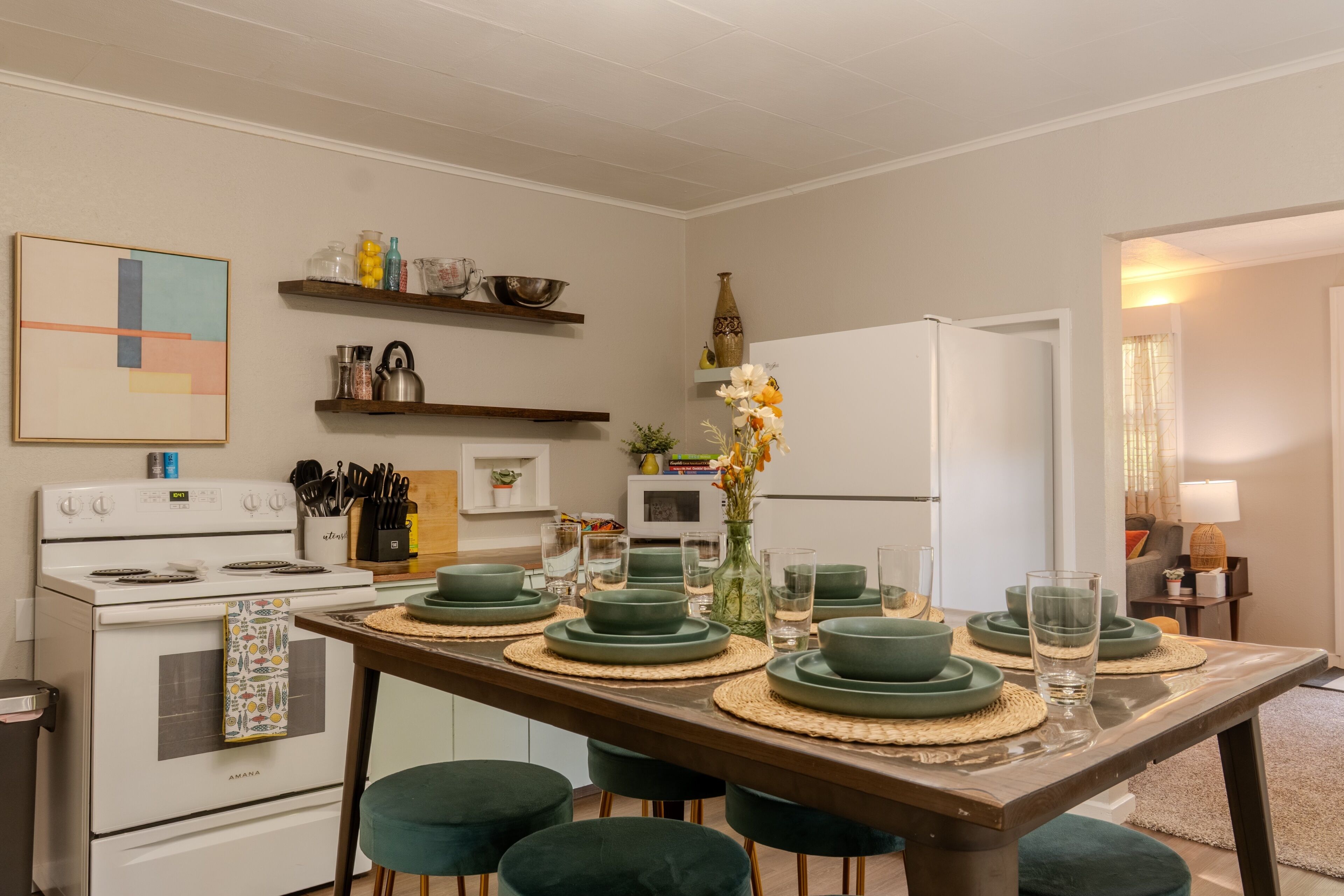 A modern kitchen with a dining table set for four, equipped with green plates and bowls, and a refrigerator in the background.