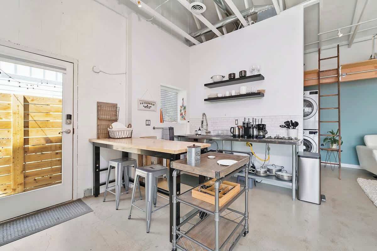 Una cucina funzionale con un tavolo di legno, sgabelli, un carrello in metallo e una lavatrice.