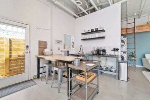 Uma cozinha compacta com uma mesa de madeira, banquetes, um carrinho de metal e uma máquina de lavar roupa.