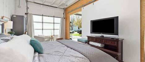 A modern bedroom with a large bed, a flat-screen TV, and a sliding door leading to an outdoor area.