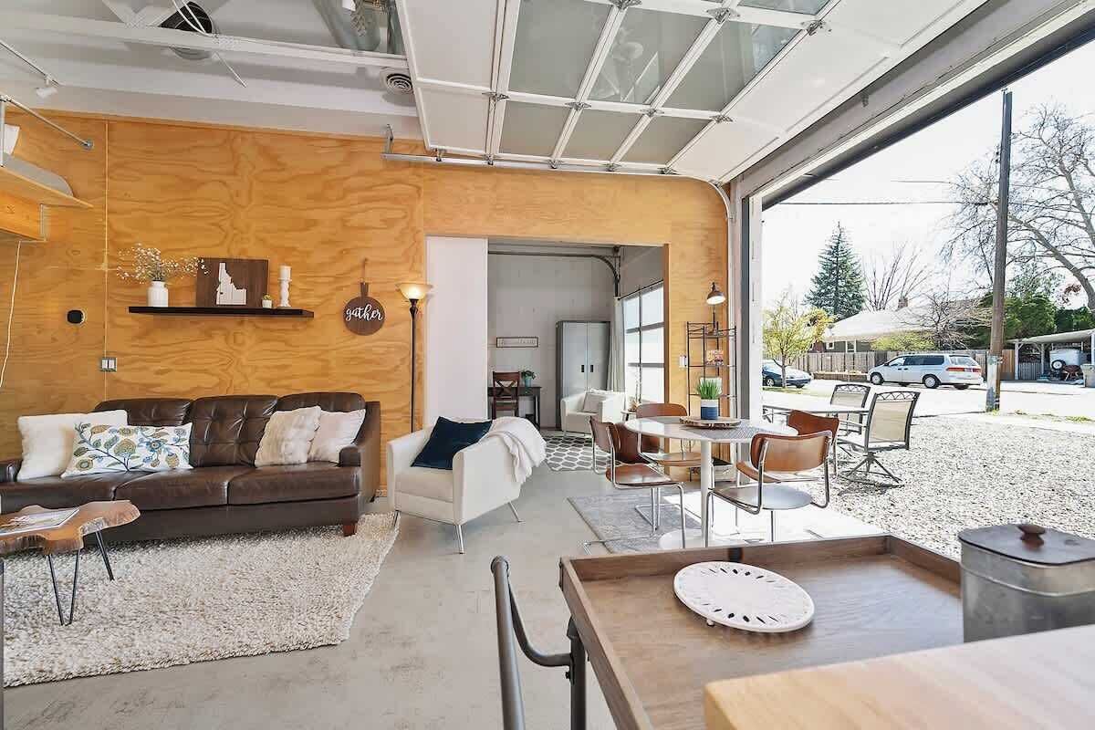 A modern interior with a wooden accent wall, a leather sofa, a dining area with chairs, and a view of the outside.