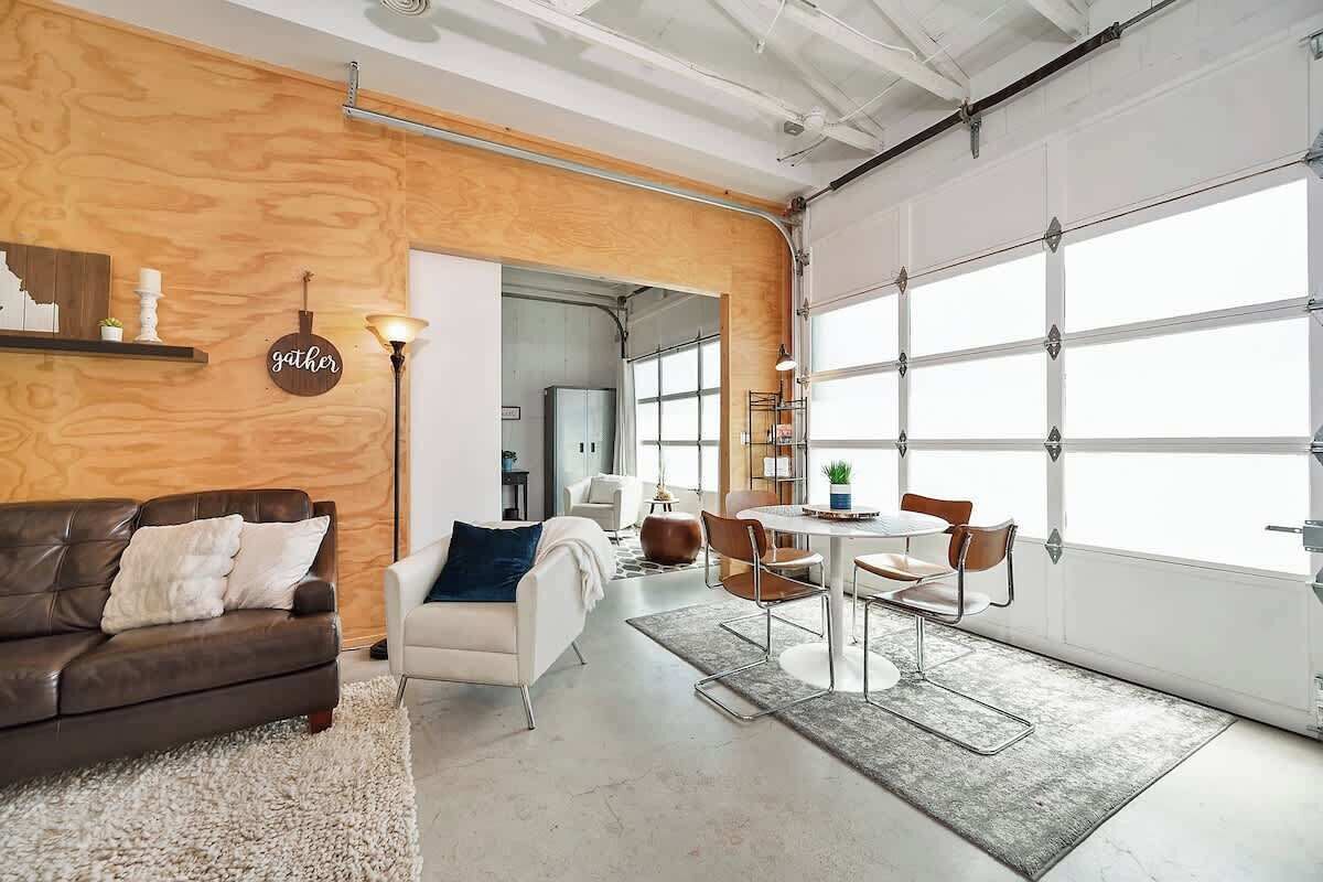 A modern interior with a wooden accent wall, a white sofa, a dining area with chairs, and a large garage door.