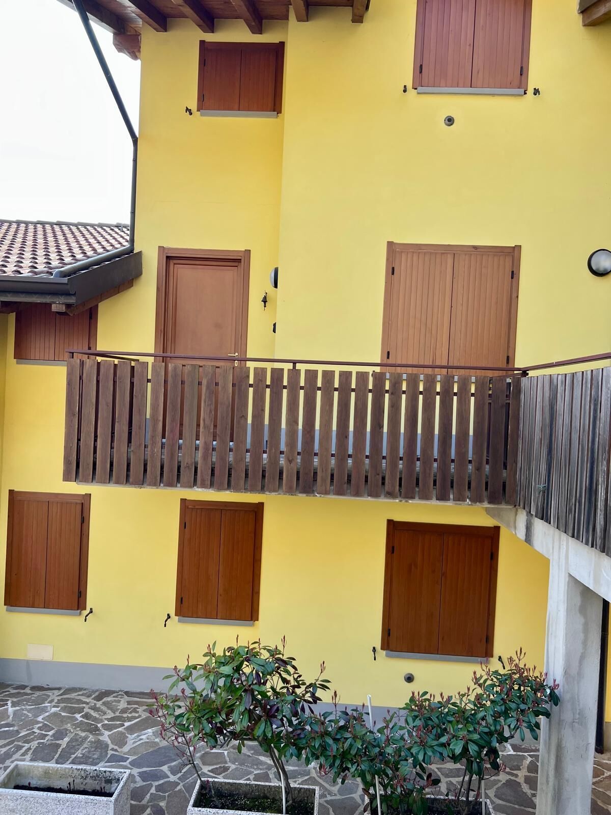 Un edificio amarillo con varias puertas y ventanas de madera, piso de piedra y una cerca de madera.
