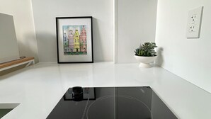Ett kök med en svart induktionshäll, ett inramat konstverk som föreställer en stadsbild, en liten krukväxt och en vit bänkskiva.