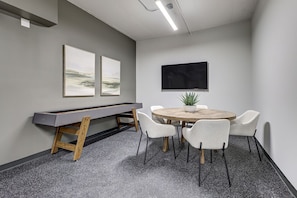 A conference room with a pool table, a round table with chairs, and two framed artworks on the wall.
