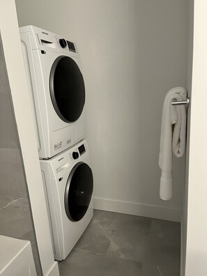 A laundry room with two stacked washers and dryers, a towel rack, and a tiled floor.