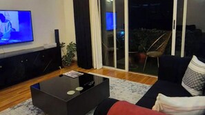 A living room with a flat-screen TV, a coffee table, a sofa, and a sliding glass door leading to an outdoor area with plants. - Cozy Two bedroom apartment in Rossyn
This property is close to UN and VillageMkt (Nairobi)