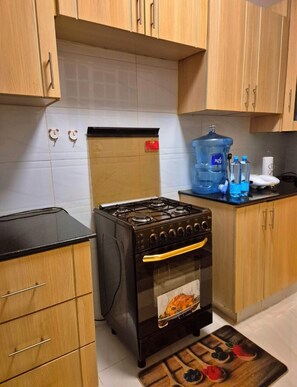 A kitchen with wooden cabinets, a black stove, and a water dispenser. - Cozy Two bedroom apartment in Rossyn
This property is close to UN and VillageMkt (Nairobi)