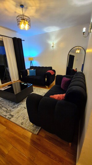A modern living room with a black sofa, a coffee table, and a large mirror. - Cozy Two bedroom apartment in Rossyn
This property is close to UN and VillageMkt (Nairobi)